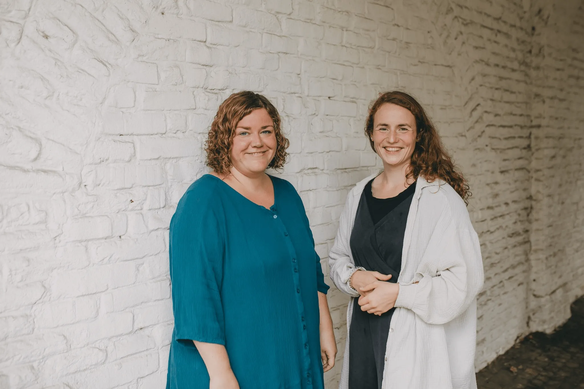 Portraitfoto von Rebekka Gohla und Ilka Tran Anh vor einer beigen Ziegelwand